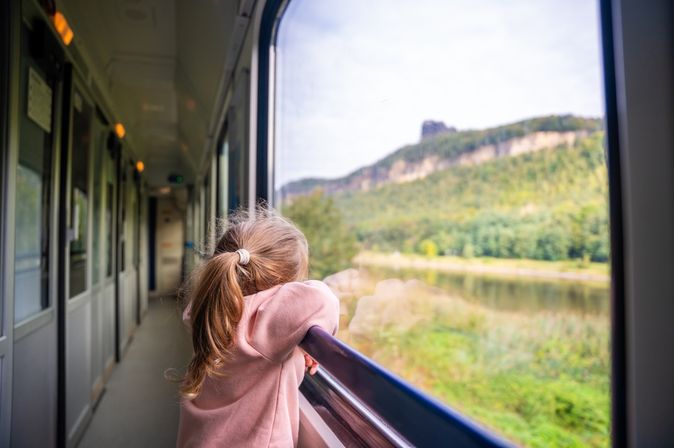 Ein Kind steht am Fenster in einem Zug und schaut auf die grüne Landschaft