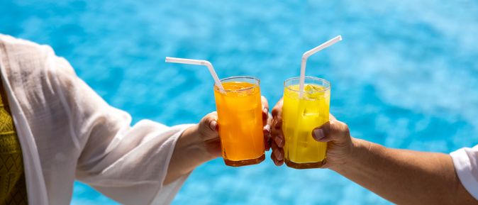 Zwei Hände stoßen mit Gläsern über einem Pool an