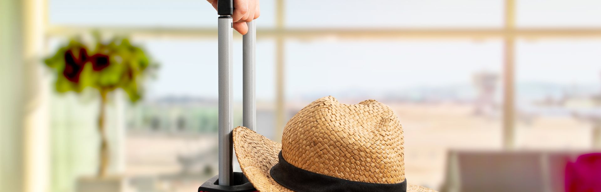 Eine Hand schiebt einen Roten Koffer auf dem ein Sonnenhut liegt