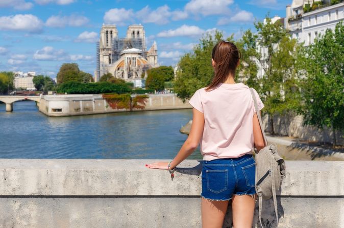 Eine Frau steht an einer Brücke und schaut auf das Wasser, im Hintergrund Bauwerke