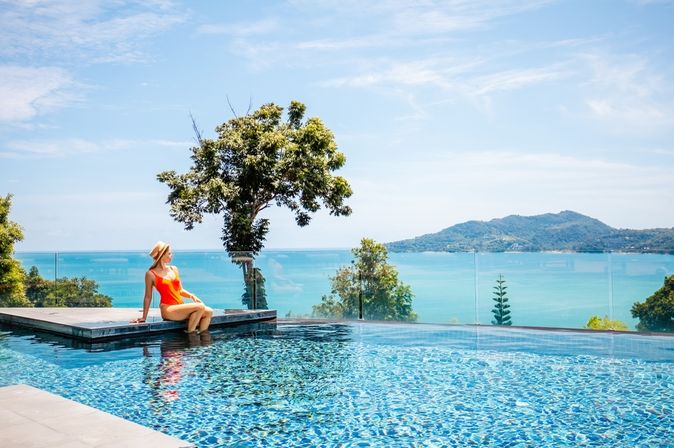 Eine Frau sitzt am Rand eines Infinity Pools mit Blick auf das Meer