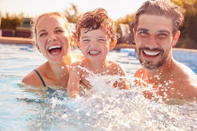 Eltern mit einem Kind spielen im Pool und lachen in die Kamera