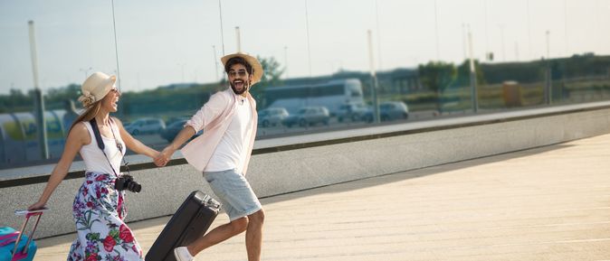 Ein Paar läuft mit Koffern aufgeregt einen Weg entlang