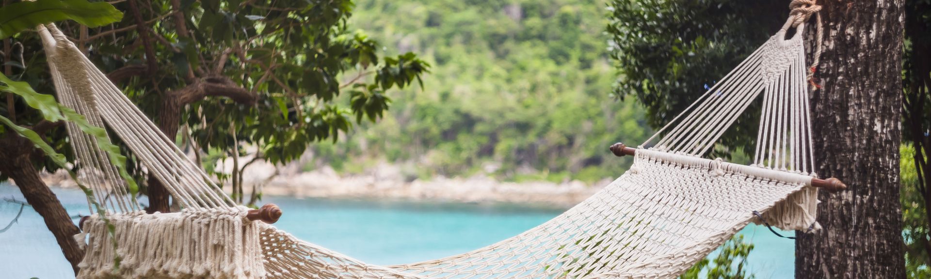 Hängematte zwischen zwei Bäumen, im Hintergund sieht man das Meer