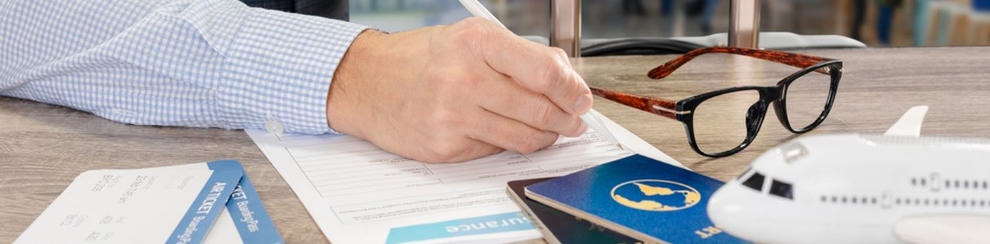 Eine Person sitzt vor einem Tisch und schreibt auf einem Blatt Papier, in der anderen Hand hält die den Griff eines Koffers fest. Auf dem Tisch liegen Flugtickets, eine Brille und zwei Reisepässe