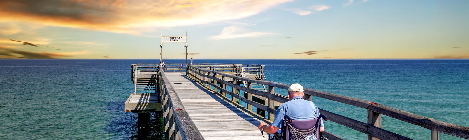 Mann im Rollstuhl auf einer Seebrücke am Meer