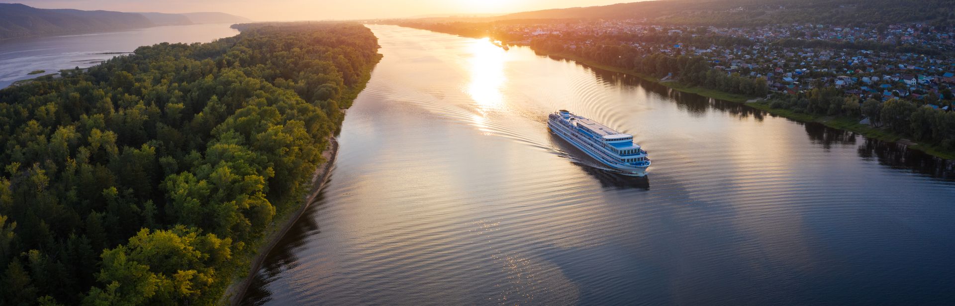 Flusskreuzfahrtschiff, dass bei Sonnenuntergang auf einem Fluss fährt