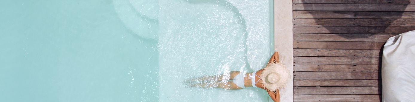 Eine Frau mit weißem Sonnenhut lehnt am Rand eines eleganten Pools