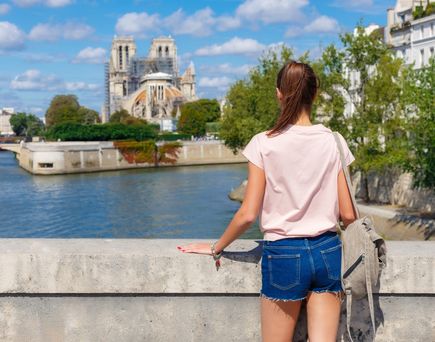 Eine Frau steht an einer Brücke und schaut auf das Wasser, im Hintergrund Bauwerke