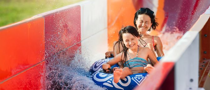 Eine Frau und ein Kind rutschen auf einem Reifen eine rote Wasserrutsche