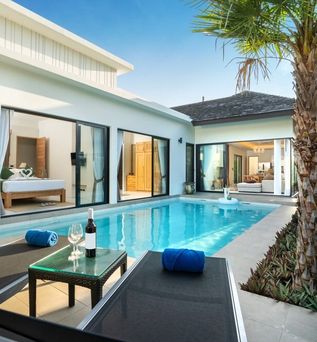 Ein Pool vor einer eleganten Villa mit zwei Liegen und einem Tisch
