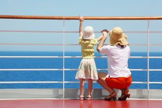 Mutter und Kind stehen an der Reling von einem Kreuzfahrtschiff und schauen auf das Meer