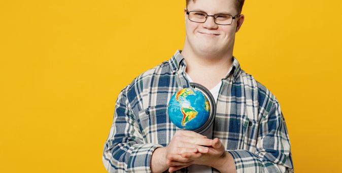 Mann mit Down-Syndrom hält eine Weltkugel in den Händen und lächelt in die Kamera