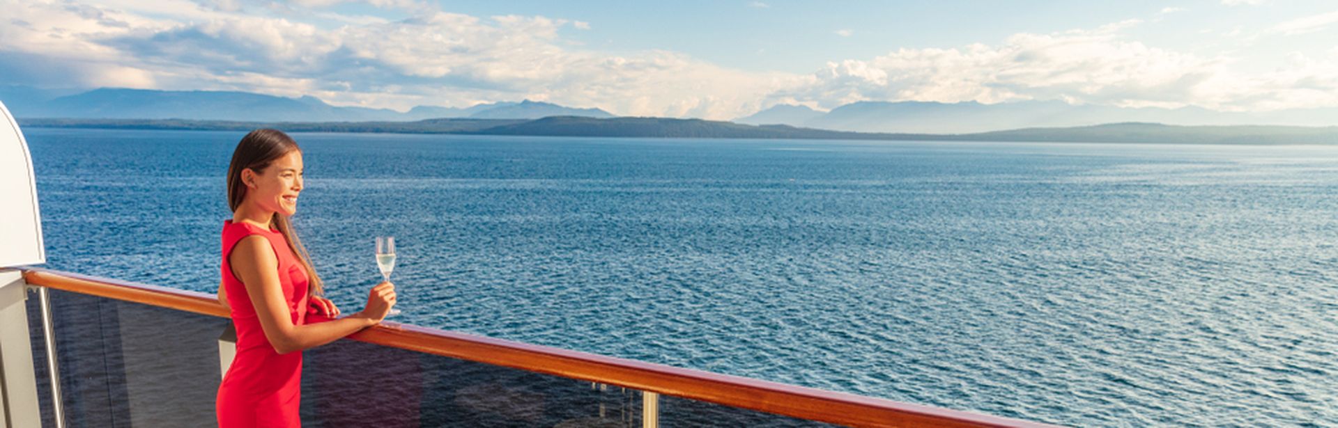 Eine Frau steht mit einem Glas Sekt auf einem Balkon eines Kreuzfahrtschiffes