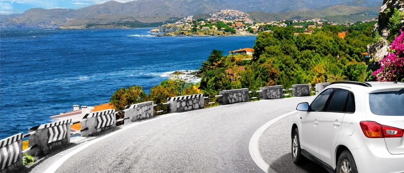 Ein weißes Auto fährt eine scharfe Kurve am Meer entlang