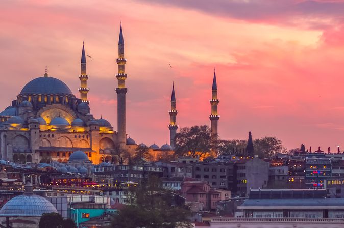 Bauwerk mit einer größeren Kuppel und einigen hohen, schmalen, runden uns spitzen Türen in mitten einer Stadt bei Sonnenuntergang