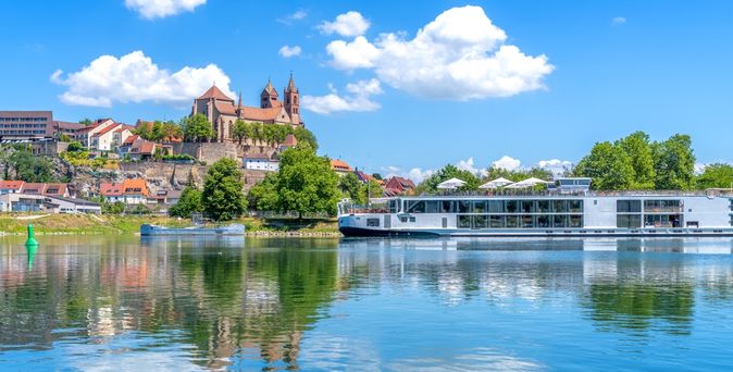 Flusskreuzfahrtschiff fährt entlang einiger Gebäude am Ufer bei Sonnenschein