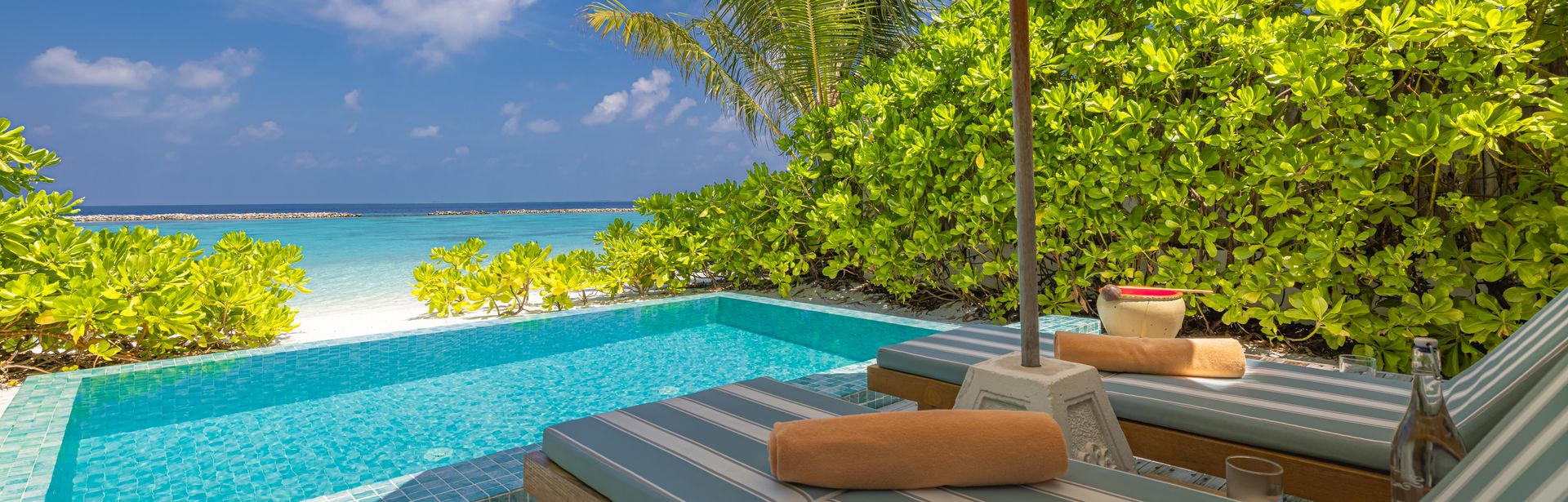 Zwei Liegen unter einem Sonnenschirm, vor einem kleinen Pool