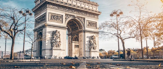 Der Arc de Triomphe im Herbst. im Vordergrund liegen braune Blätter auf dem Boden.