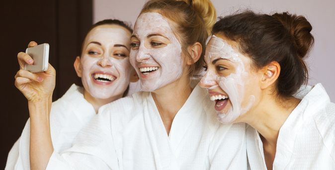 Drei Frauen tragen Gesichtsmasken und machen lachend ein Selfie