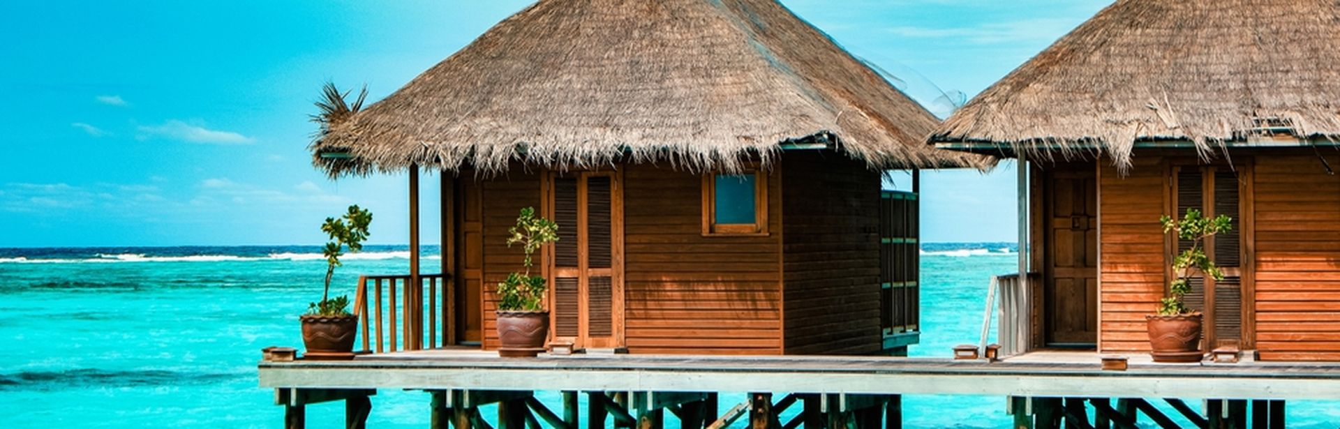 Zwei strohgedeckte Holzhütten stehen auf Stelzen über dem Meer.