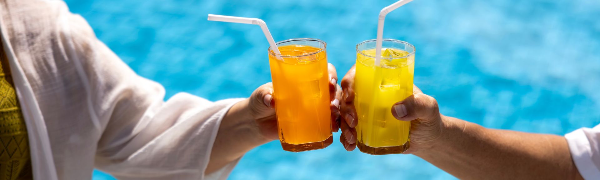 Zwei Hände stoßen mit Gläsern über einem Pool an