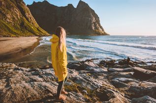 Eine Frau in einer gelben Regenjacke schaut auf das Meer