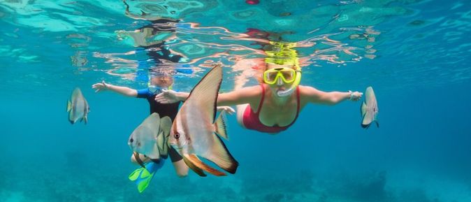 Zwei Kinder tauchen mit Taucherbrille und Schnorchel zwischen Fischen