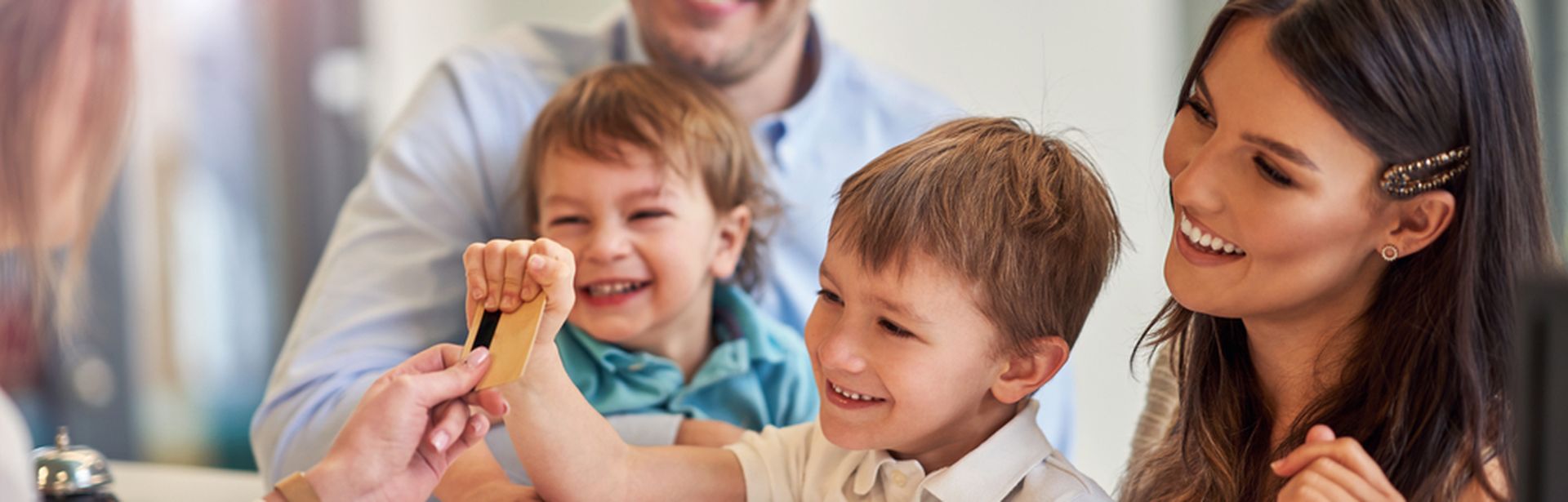 Eine Familie mit zwei Kindern beim Check-In, die Rezeptionistin reicht dem kleinen Kind die Zimmerkarte