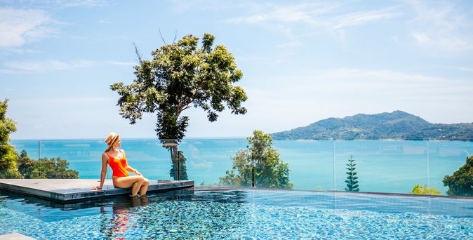Eine Frau sitzt am Rand eines Infinity Pools mit Blick auf das Meer