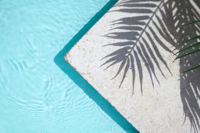 Pool von oben, auf dem Rand sieht man den Schatten einer Palme