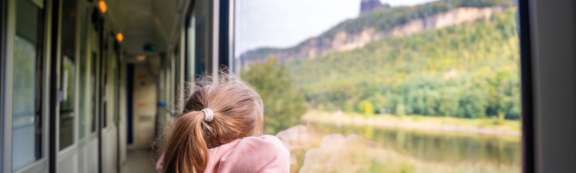 Ein Kind steht am Fenster in einem Zug und schaut auf die grüne Landschaft