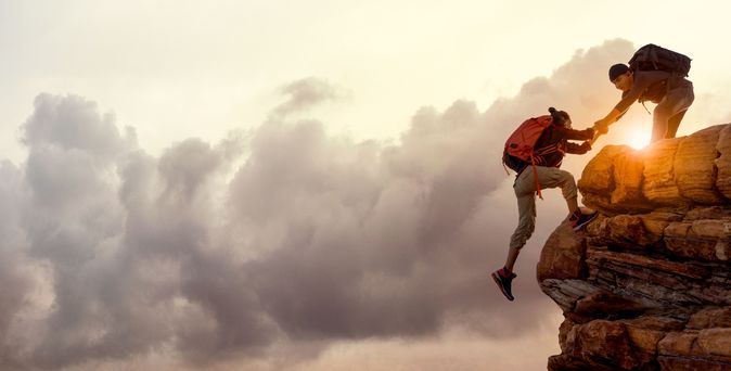 Wanderer bei Sonnenaufgang, Mann hilft Frau einen Berg hoch