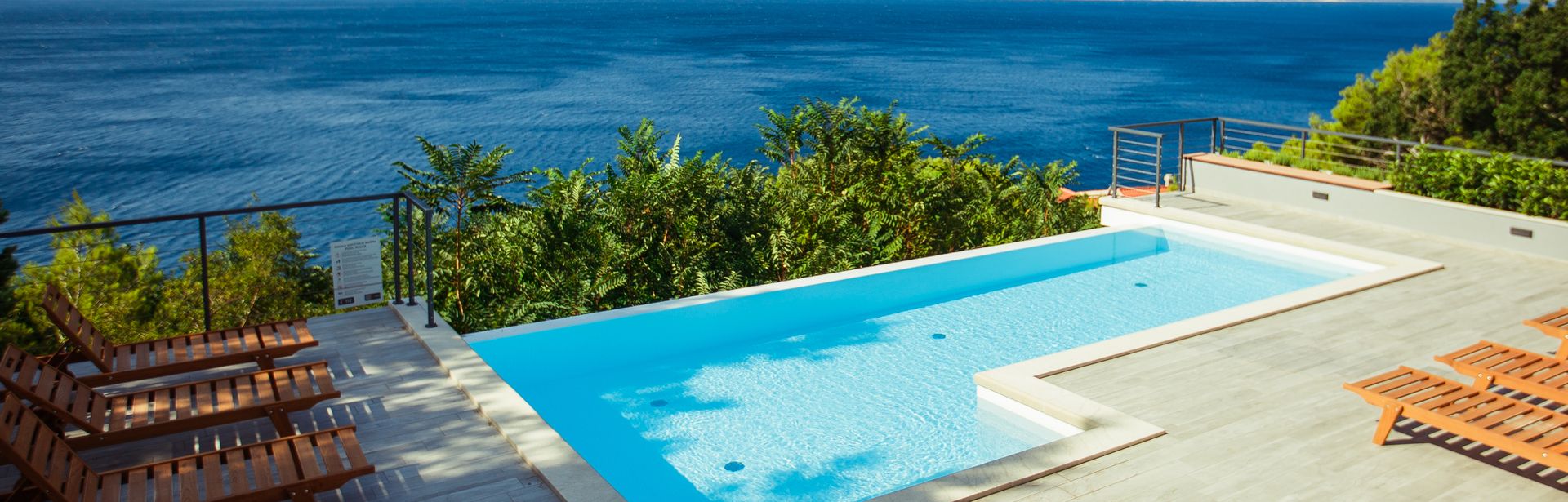 Ein Privatpool über dem Meer, um ihn herum einige Holzliegen und Bäume
