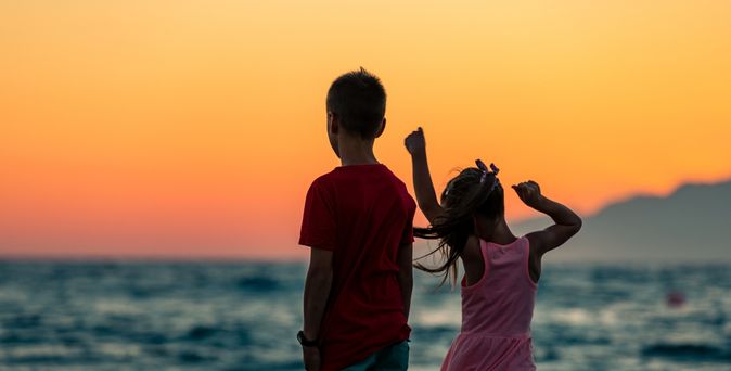 Zwei Kinder schauen bei Sonnenuntergang aufs Meer