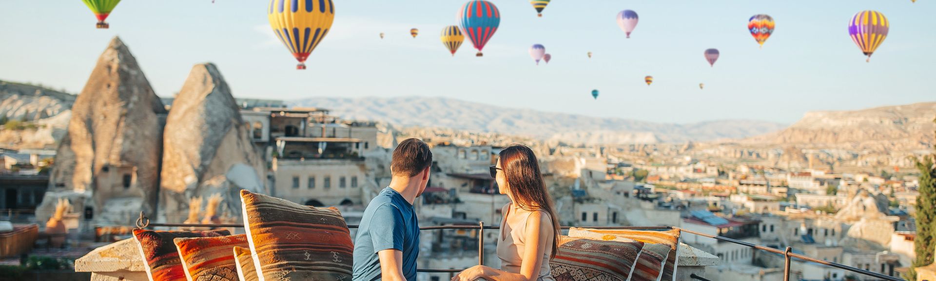 Fröhliches junges Paar beim Sonnenaufgang mit Heißluftballons in Kappadokien