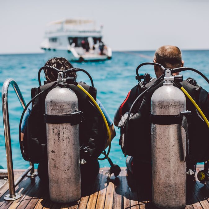Taucher sitzen mit Tauchausrüstung am Wasser