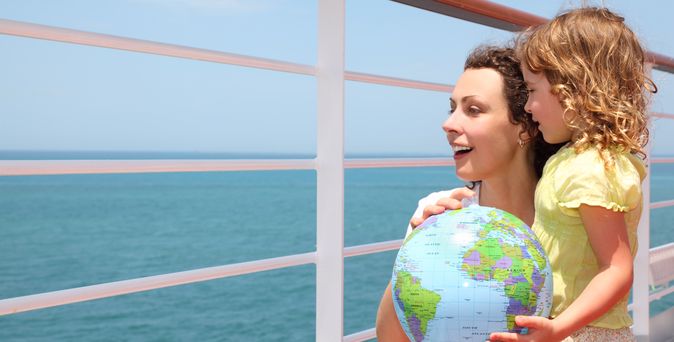 Mutter und Kind schauen über das Geländer eines Kreuzfahrtschiffes und halten einen Globus
