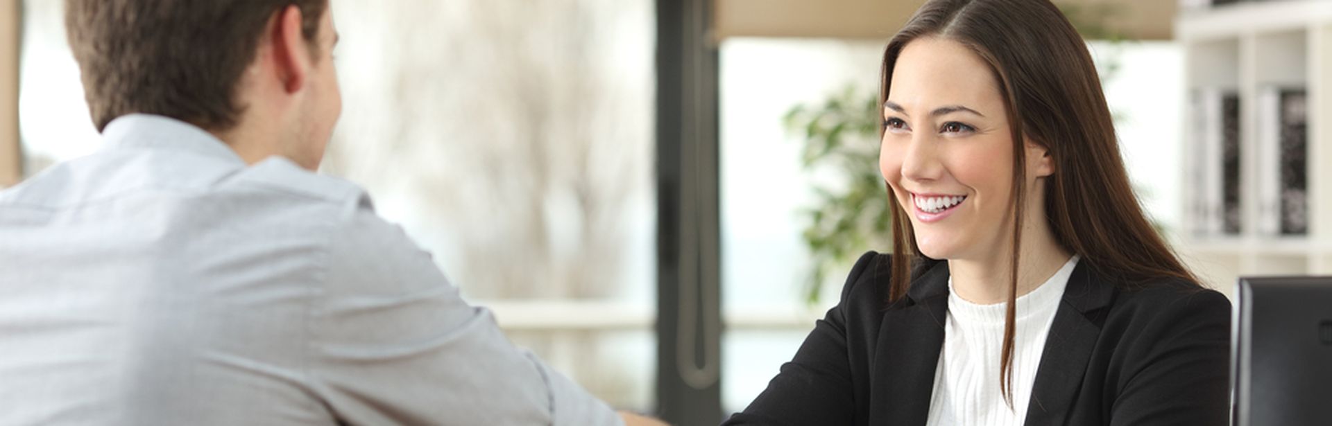 Eine Frau sitzt an einem Schreibtisch. Ihr gegenüber sitzt ein Mann und die beiden geben sich die Hand