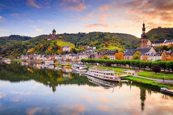 Schiffe am Ufer der Mosel mit Häusern und Sonnenuntergang im Hintergrund