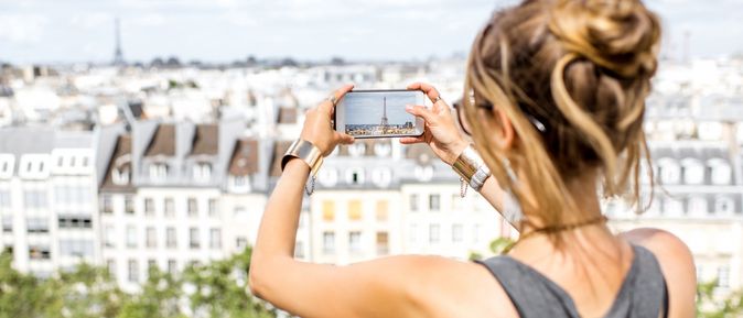 Eine Frau macht mit ihrem Handy ein Foto von einer Stadt, welche sie von einem höher gelegenen Aussichtspunkt betrachtet