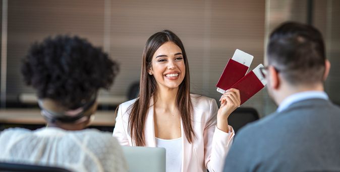 Eine lächelnde Reiseberaterin hält Ihren Kunden zwei Reisepässe mit Flugtickets hin