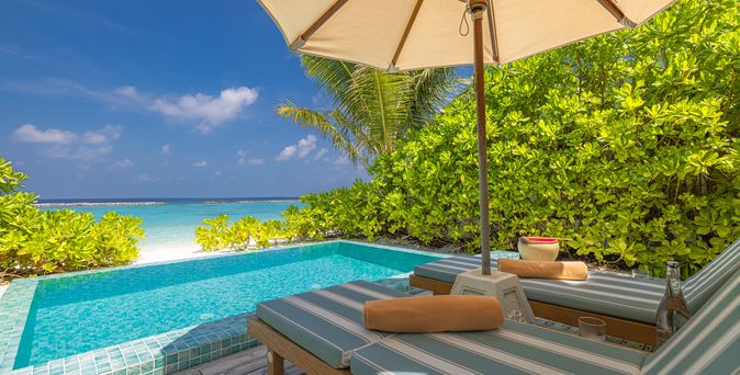 Zwei Liegen unter einem Sonnenschirm, vor einem kleinen Pool