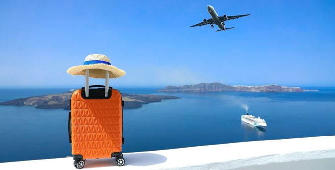 Ein Koffer steht auf einer Mauer, im Hintergrund sieht man das Meer und ein Schiff, im Himmel fliegt ein Flugzeug