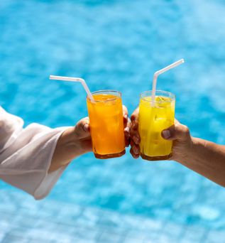 Zwei Hände stoßen mit Gläsern über einem Pool an