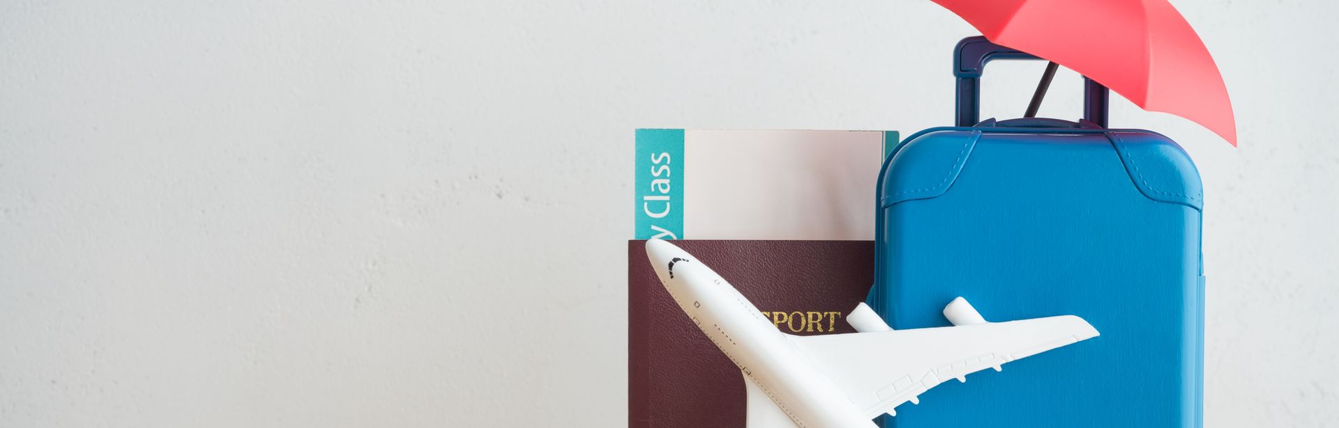 Ein Spielzeugkoffer, ein Spielzeugsonnenschirm, ein Spielzeugflugzeug, ein Reisepass und eine kleine Weltkugel stehen auf einem Tisch