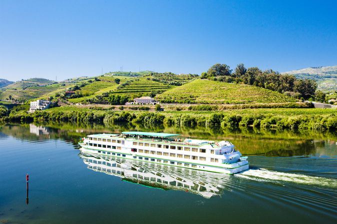 Flusskreuzfahrtschiff, dass durch eine hüglige, grüne Landschaft fährt