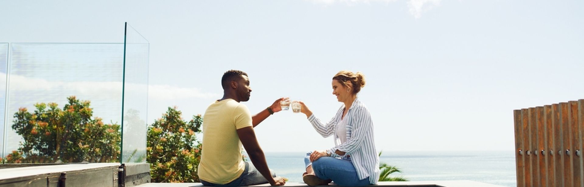 Eine Frau und ein Mann sitzen am Pool und stoßen mit Ihren Getränken an