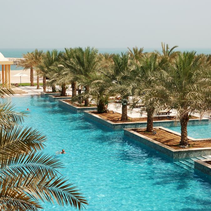 Poollandschaft mit Palmen und Blick auf das Meer