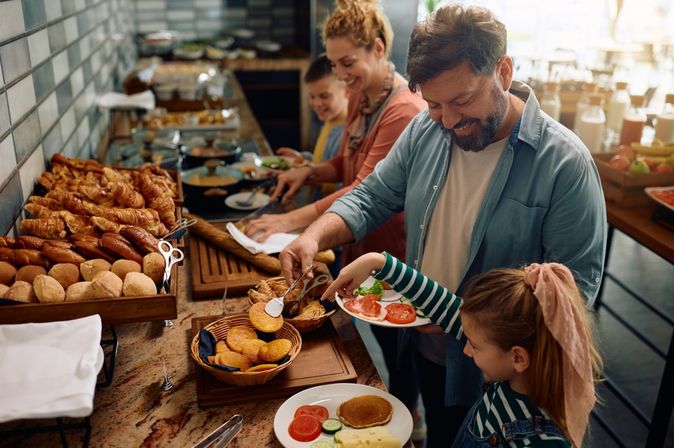 Eine Familie bedient sich lachend an einem Frühstücksbuffet